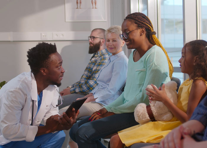 A doctor kneeling while talking to patients sitting in a waiting room.