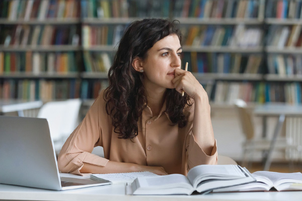 Female student sitting at a desk with a laptop and looking pensively off in the distance.
