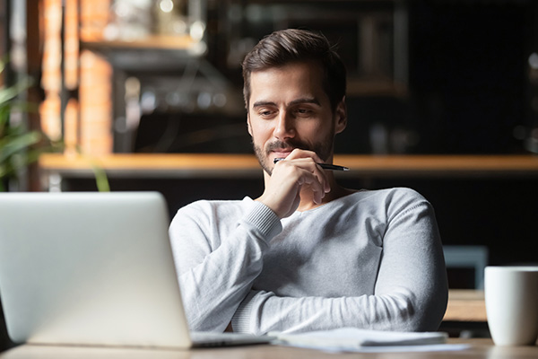 Male student looking at laptop with satisfied look on his face.