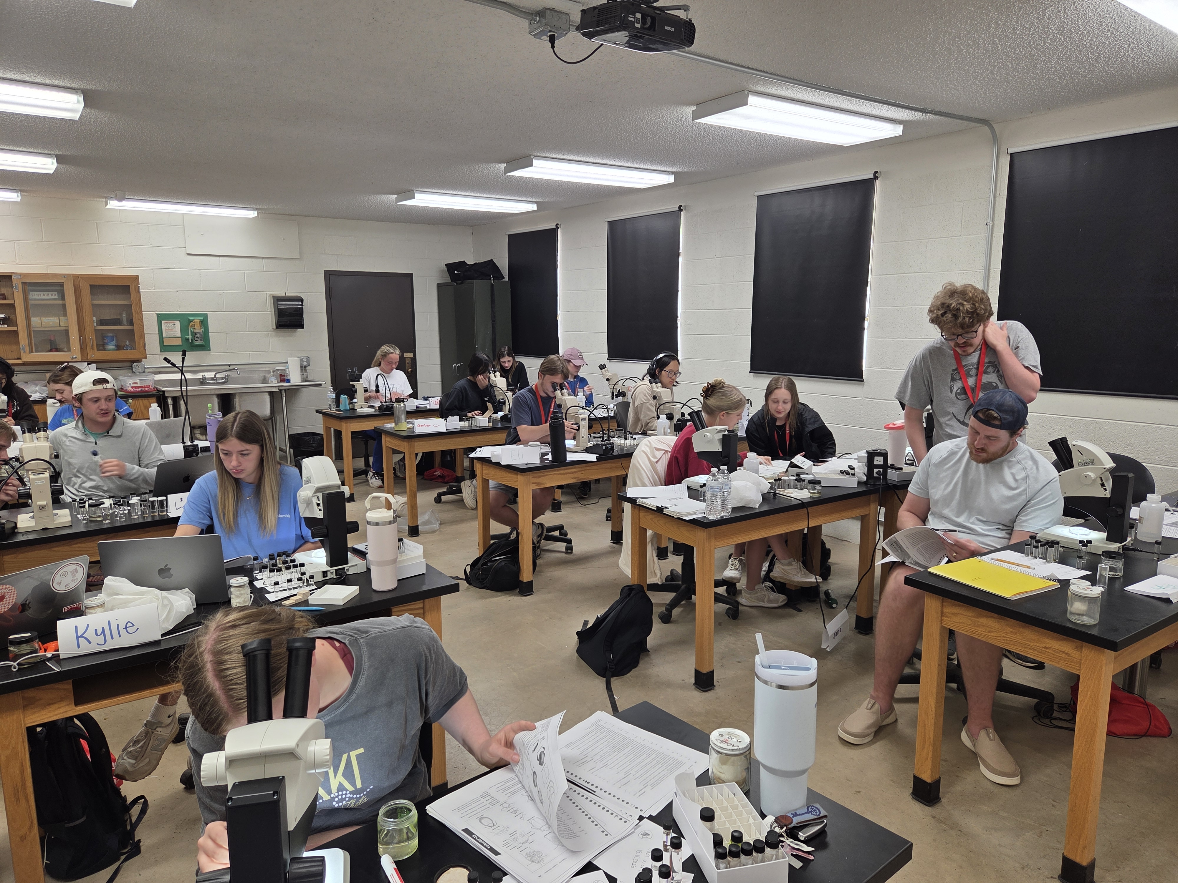 Students working with microscopes and lab materials at tables in a classroom during a hands-on science session at the biological station.