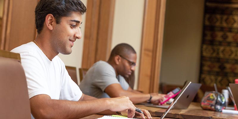 two students sit with their laptops while studying 