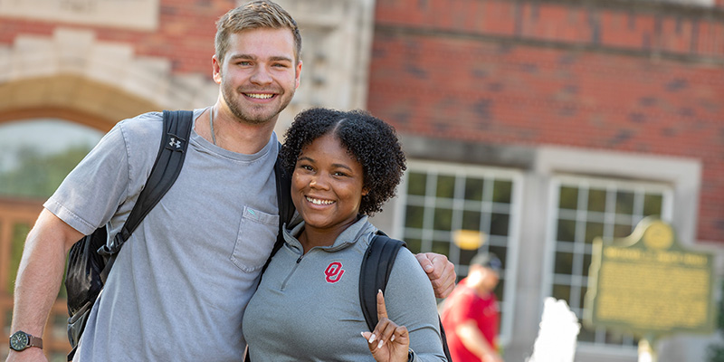 two young undergrad students pose for a photo in front of Price Hall