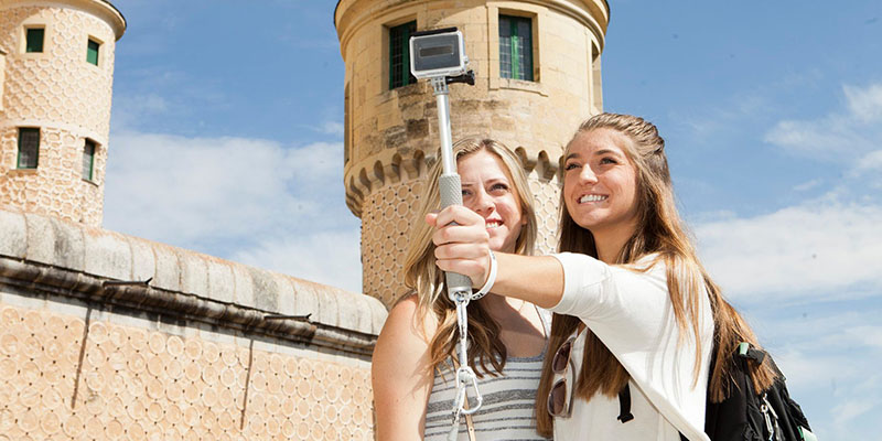 two young girls pose in front of a tourist attraction taking a photo with a selfie stick