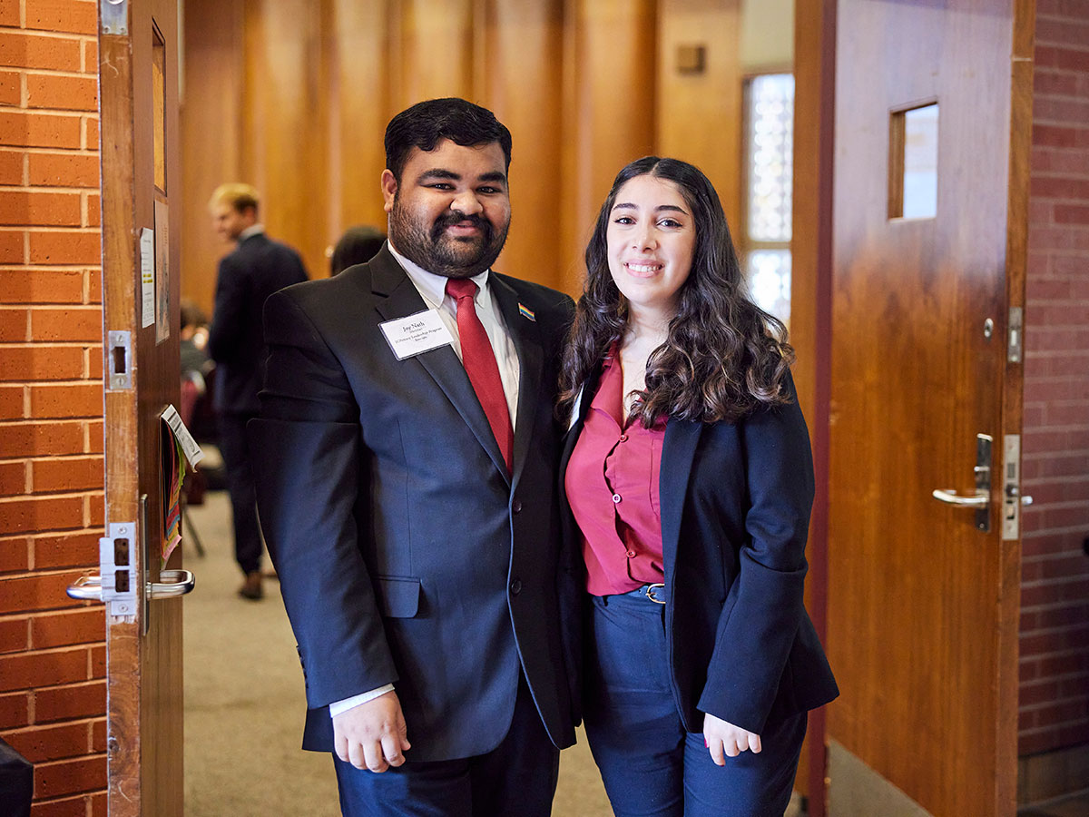 Two professionally dressed students welcome guests to the conference.