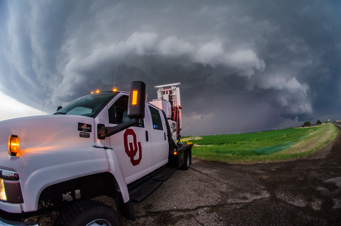 A mobile OU radar truck in the field, with a storm in the background.