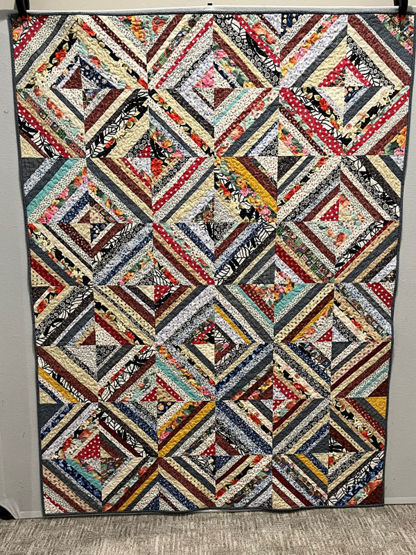 A quilt with geometric patterns forming squares and diamonds in a variety of patterns and colors.
