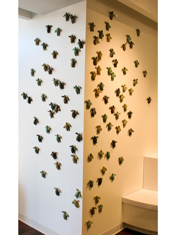 Ceramic and plexiglass sea turtles mounted along white wall climbing towards the ceiling.