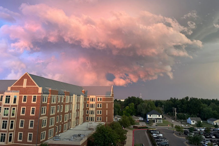 A photograph of the sun breaking through stormy clouds with contrasting greys and pink colors in the sky.