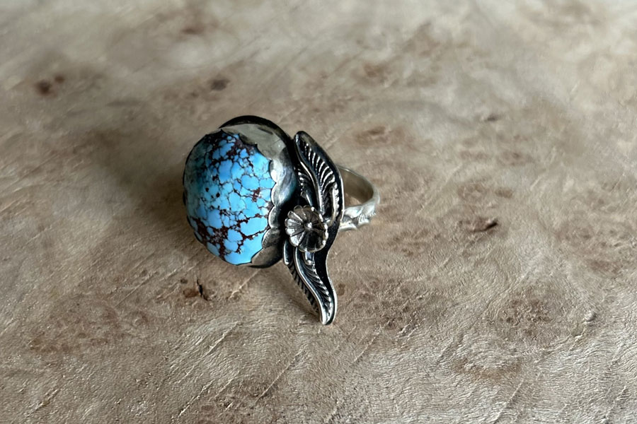 A light blue vibrant turquoise stone ring framed with feathers and flowers.