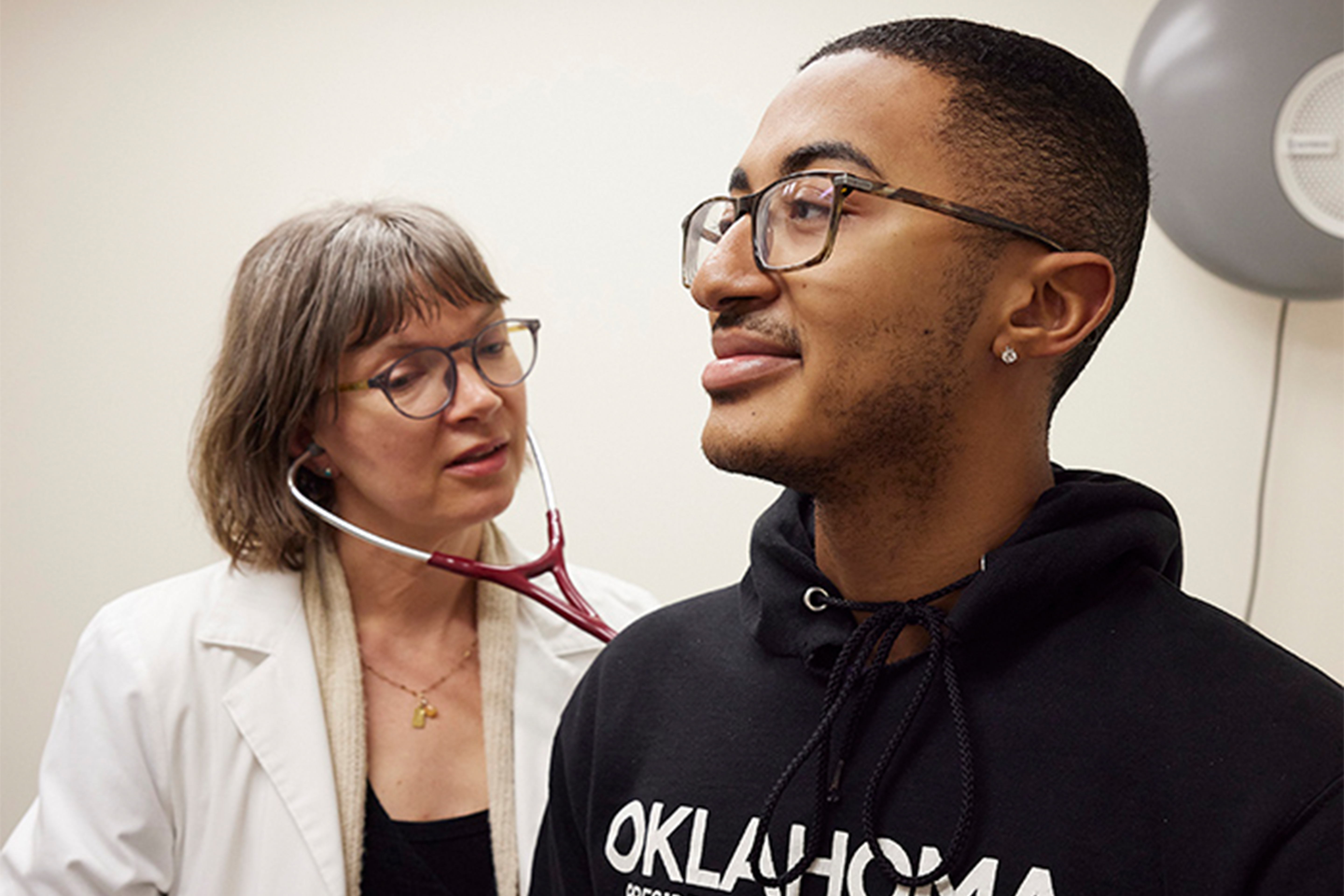 A physician using a stethoscope on a student.