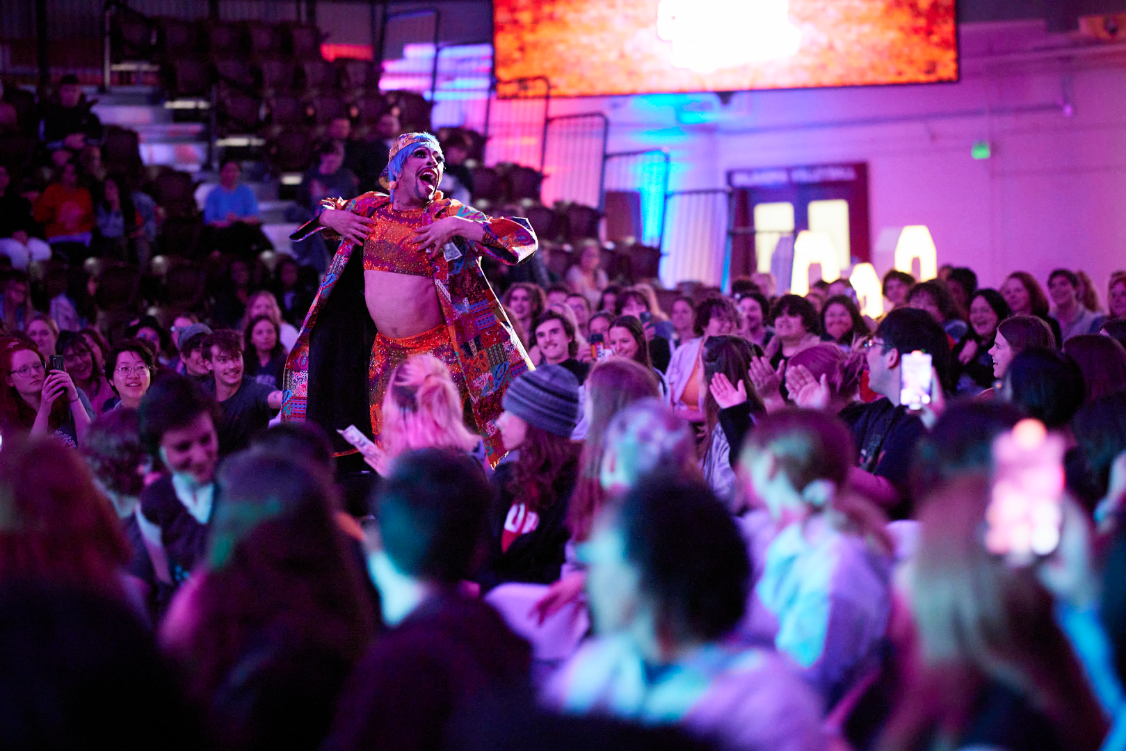 Drag performers Yvie Oddly performing in the crowd in McCasland Field House, the room has colorful lights