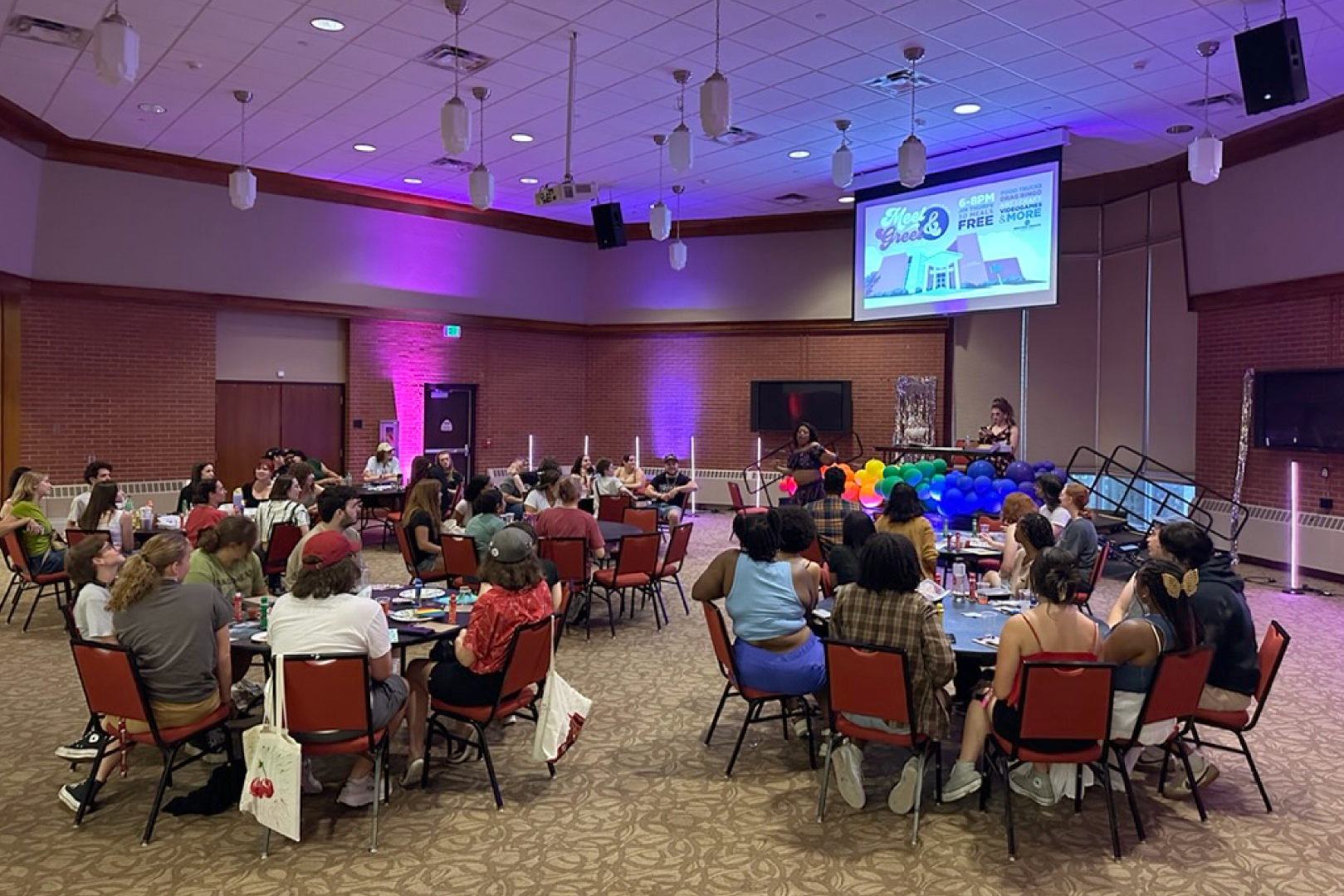 A group of students playing bingo with a drag performer in Jim Thorpe, the room has colorful lights