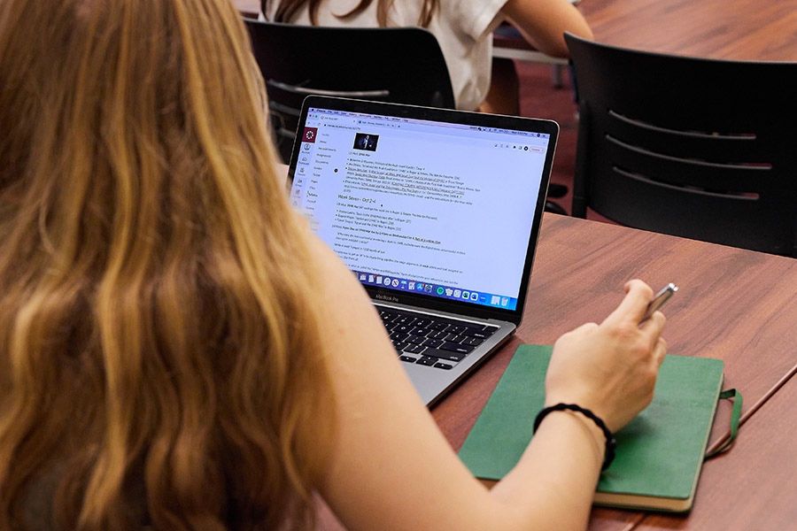 A student sits at a table looking at her laptop. 