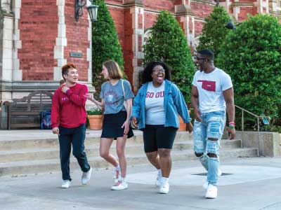 Four smiling students walking and talking on a sidewalk on OU campus.