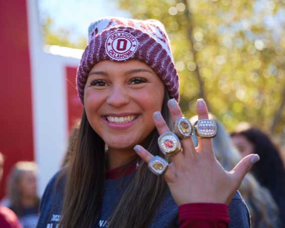 An athlete holds up her hand, on each finger is a large ornate ring from winning at sports
