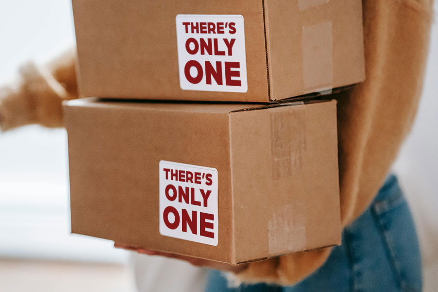 The person holding 2 cardboard boxes stacked with There's Only One stickers on them.