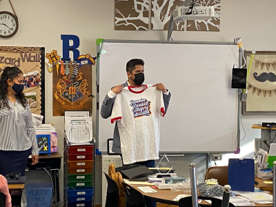 Juan holding up a JRCoE t-shirt in front of his class.