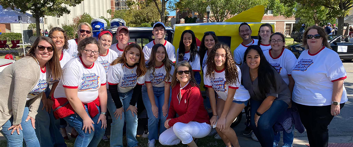Group photo of OU students and the dean in front of the golf cart for homecoming
