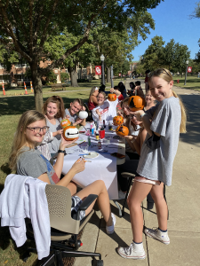 Students sitting at a table on the Sout Oval holding painted pumpkins