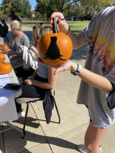 Student holding a pumpkin with a black horns down logo painted on it