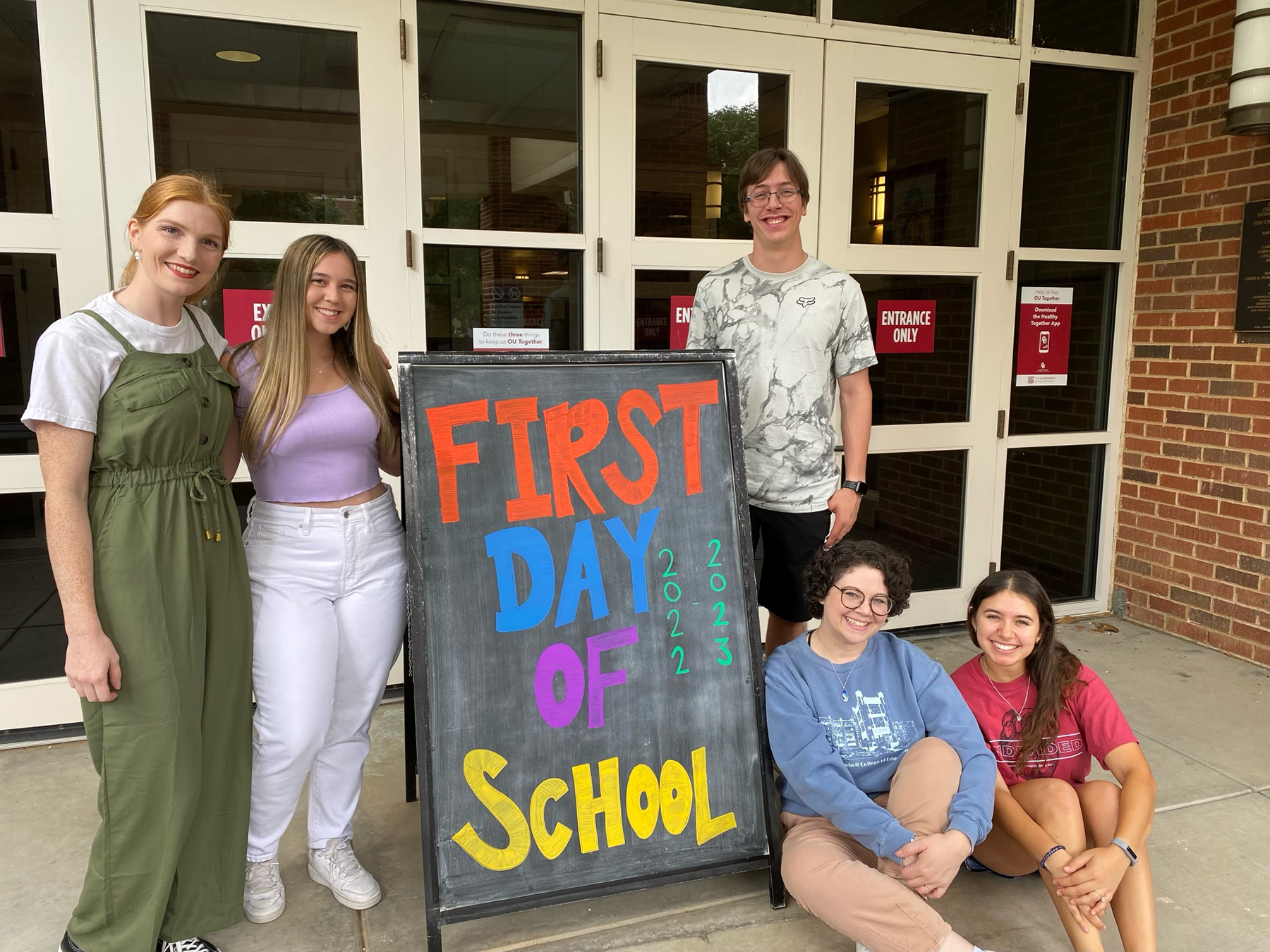 five students standing in front of collings hall with a sign that says First day of school
