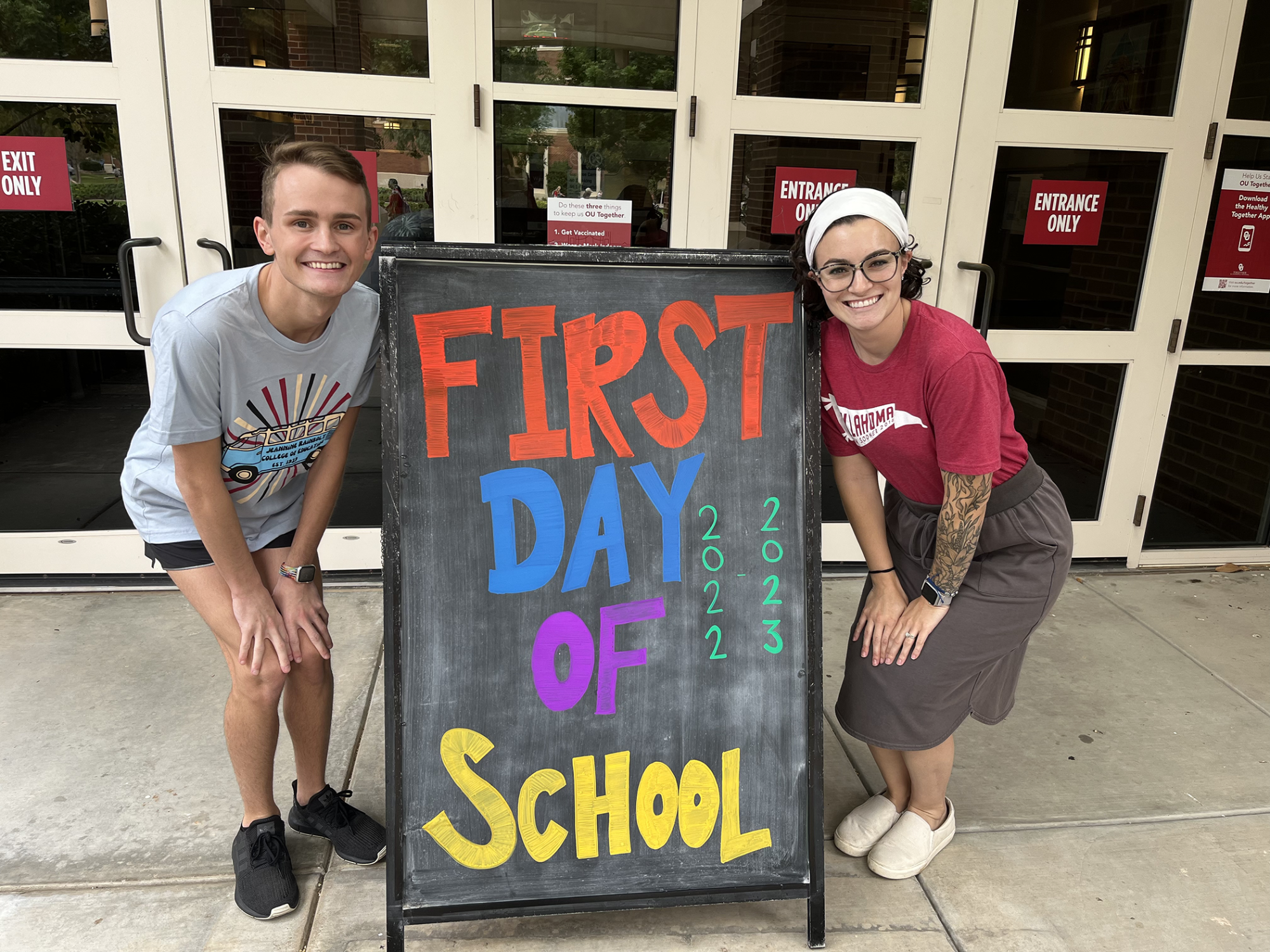 two students crouching next to a sign that says first day of school