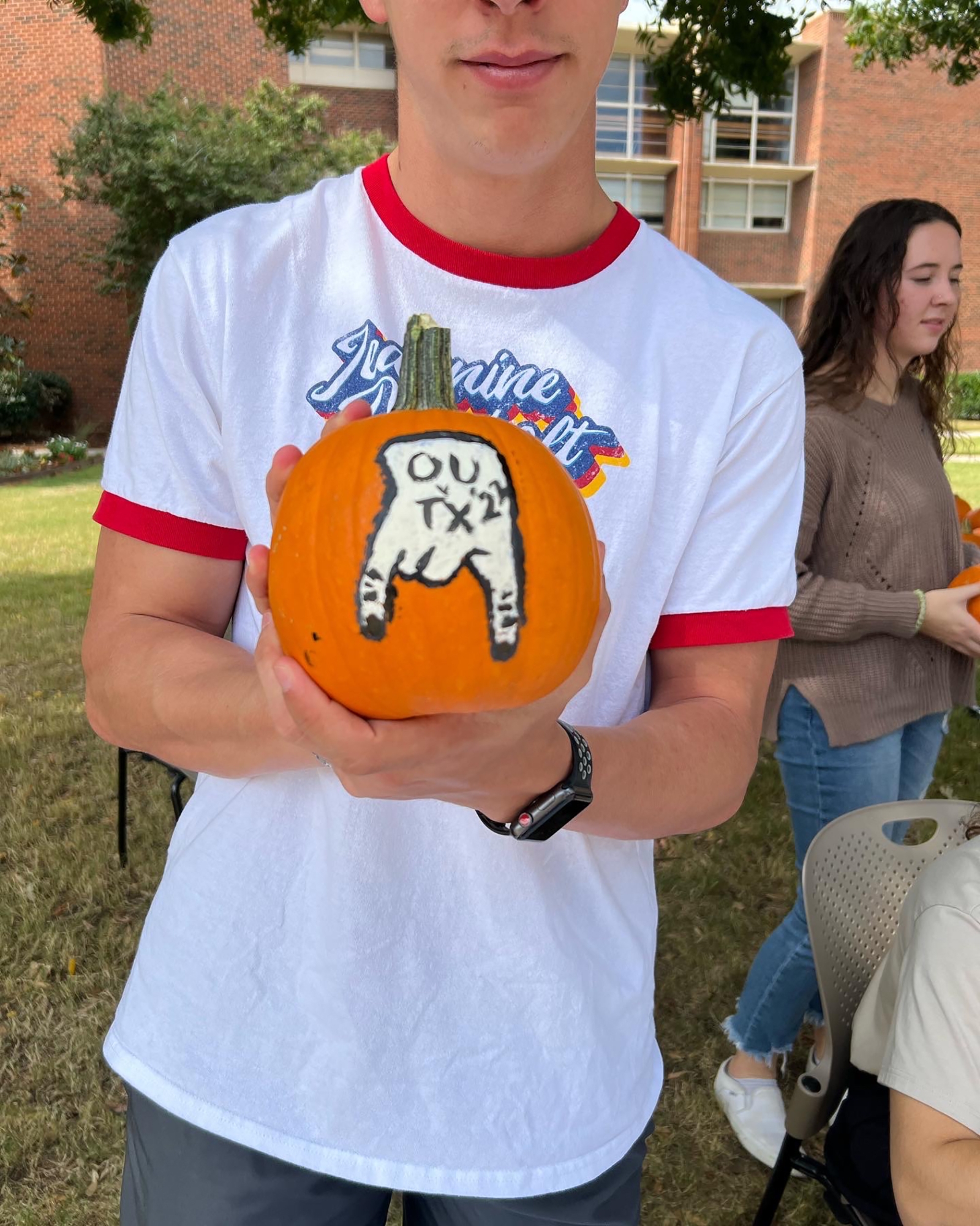 student holding a pumpkin with OU Texas and a horns down painted on the pumpkin