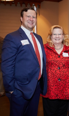 A man in a blue suite and red tie standing next to a woman in a red top with black accents. Both are smiling for the camera