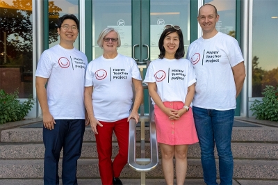four people smiling on a set of stairs. All four are wearing the same white shirt that says "Happy Teacher Project"