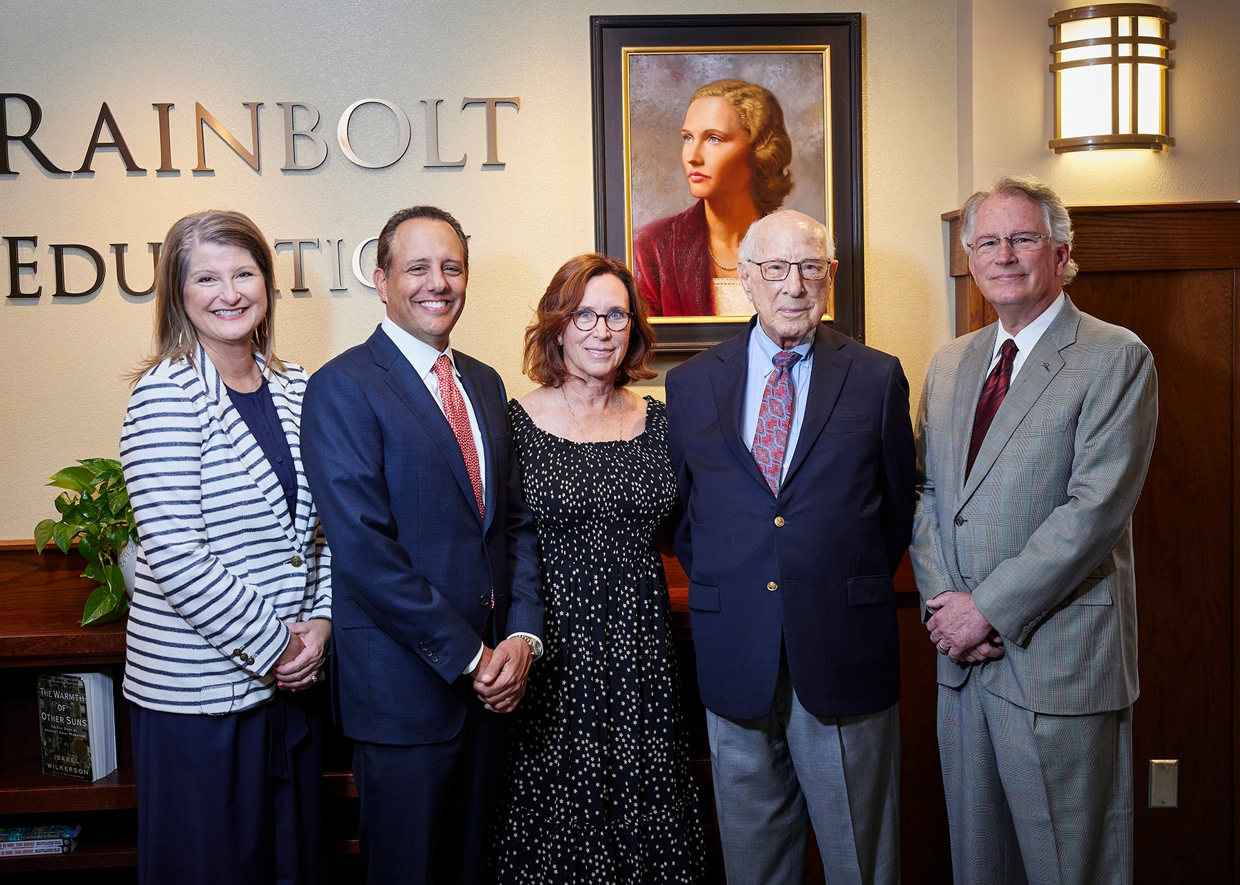 Two women and three men standing together in front of Jeannine Rainbolt portrait