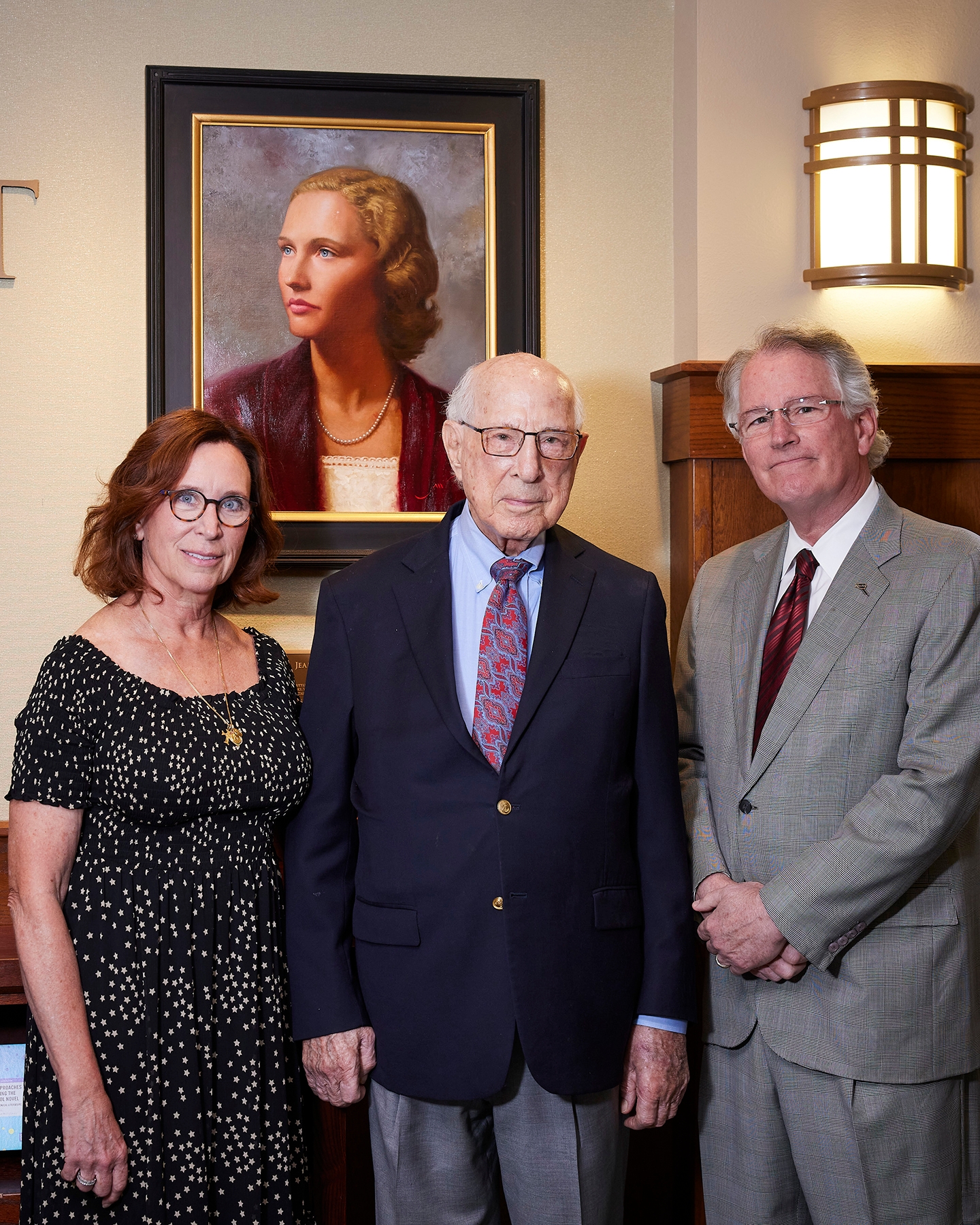 A woman and two men posing in front of a portrait on the wall