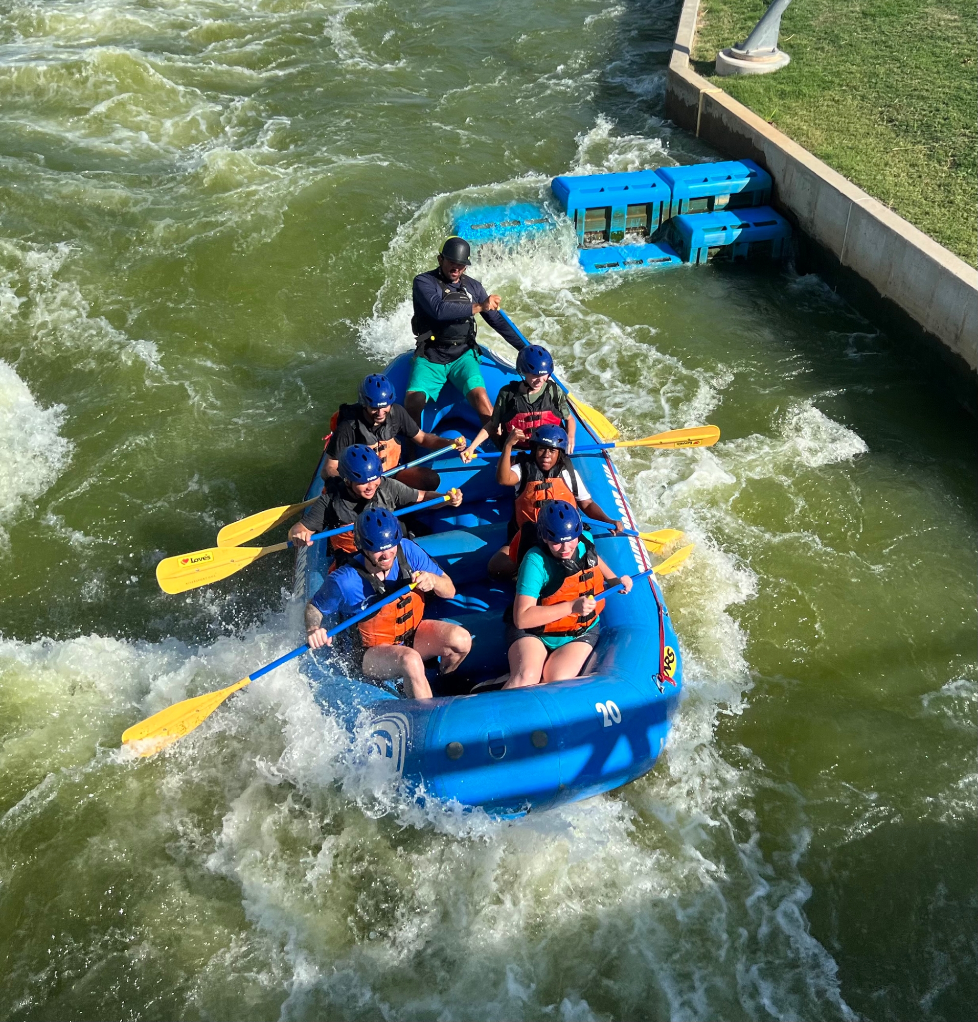 A picture from above looking down at people whitewater rafting in a blue boat