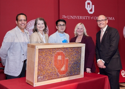 Two women and three men standing in front of a display made of pencils with the OU logo in the middle