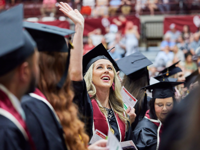 blonde woman in a cap and gown waving to the crowd at a graduation ceremony