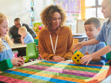 Woman in brown shirt sitting at table with 3 children who are looking at math problems on the table