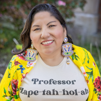 Woman wearing a yellow jacket with flowers over a t-shirt that says Professor Zape-tah-hol-ah
