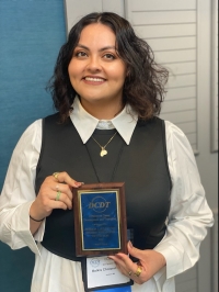 Belkis standing in front of a blue wall holding a plaque