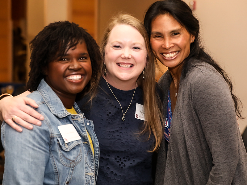 Woman in a jean jacket, woman in black and woman in a grey sweater smiling for a picture