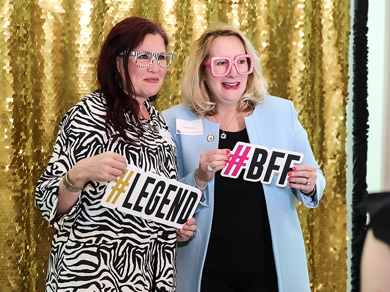 Woman in zebra print and woman in blue jacket holding funny signs at a photo booth