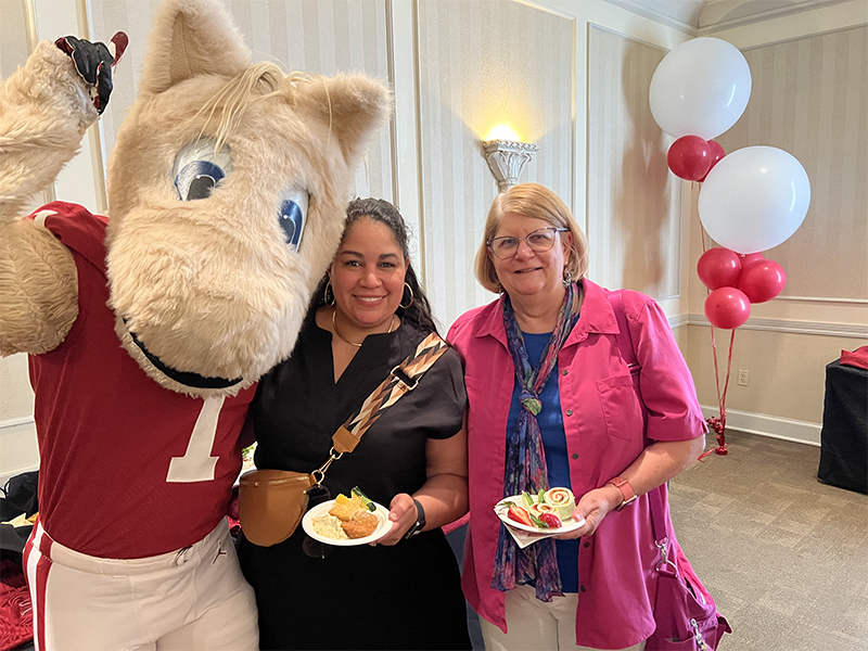 Boomer mascot standing with two women who are holding food