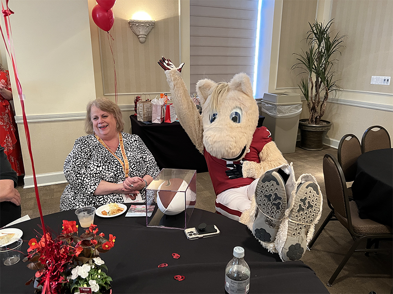 Boomer mascot sitting with feet on table next to a woman in a black and white dress