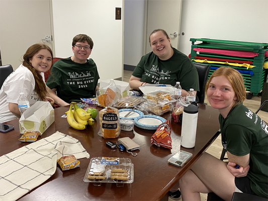 Four students sitting at a table and smiling as they eat lunch