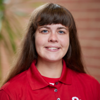 Woman with long brown hair and bangs in a red OU polo shirt