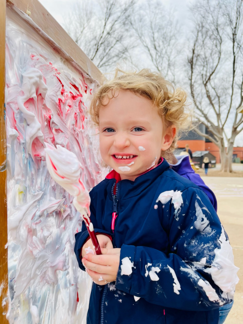 Child in a blue jacket holding a paintbrush and smiling