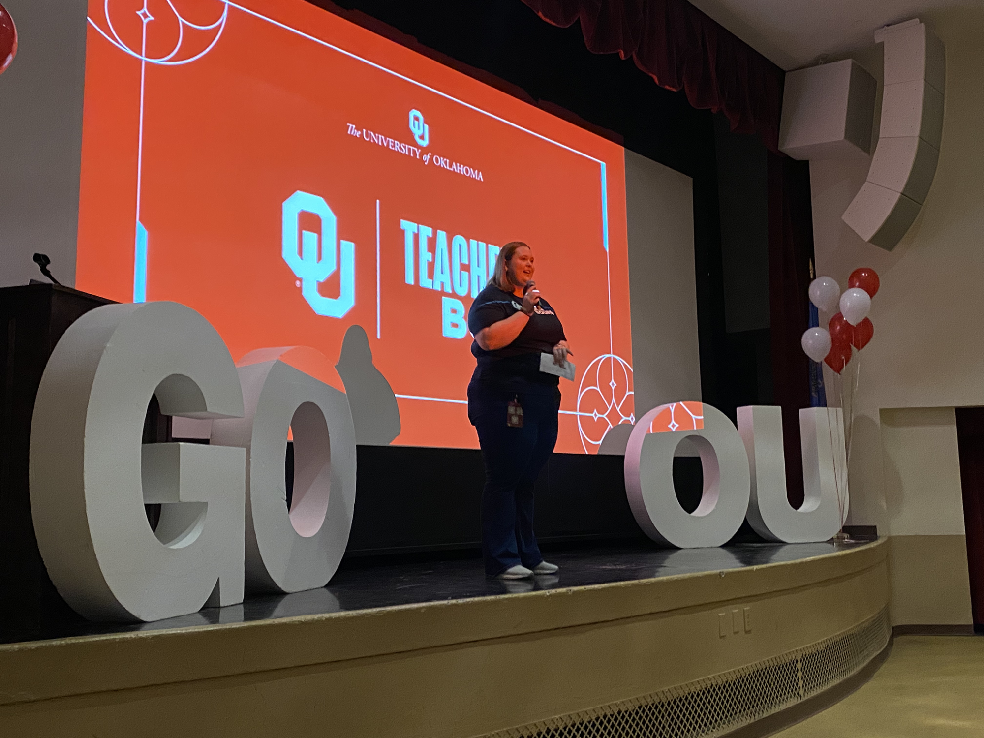 Student standing on a stage between big letters that say GO OU
