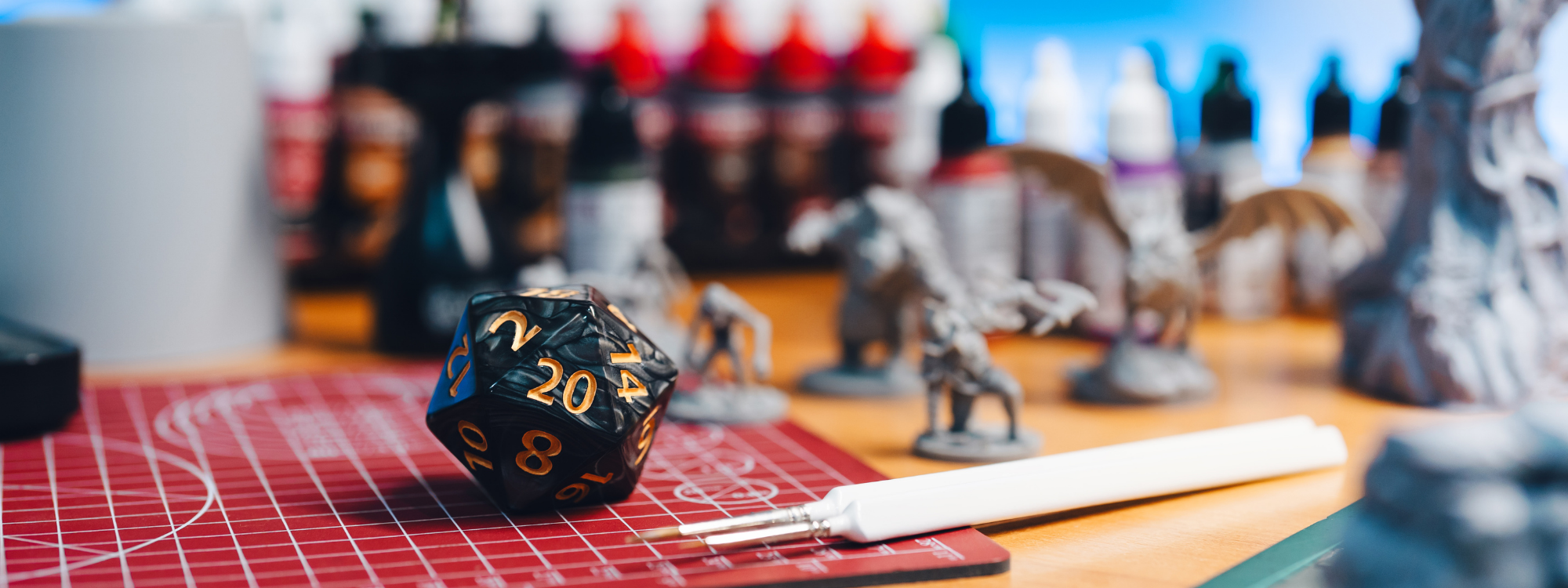 table top covered in game making supplies, journals, paints, dice, writing and cutting utensils,.