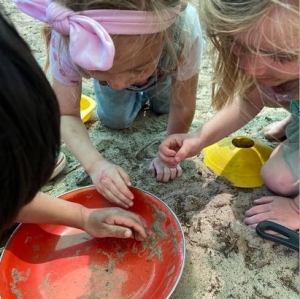 Three children kneeling in the sand and digging