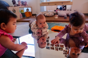 Three babies laying on a floor looking at themselves in a mirror