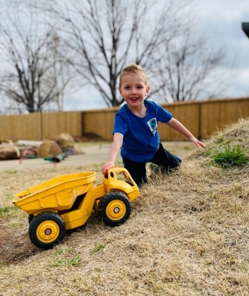 Child playing outside on a grass hill with a yellow truck