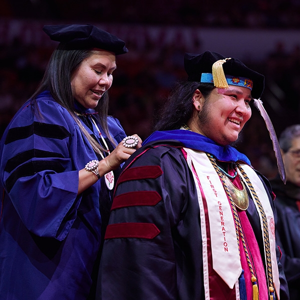 An older woman holding her diploma and smiling at graduation.